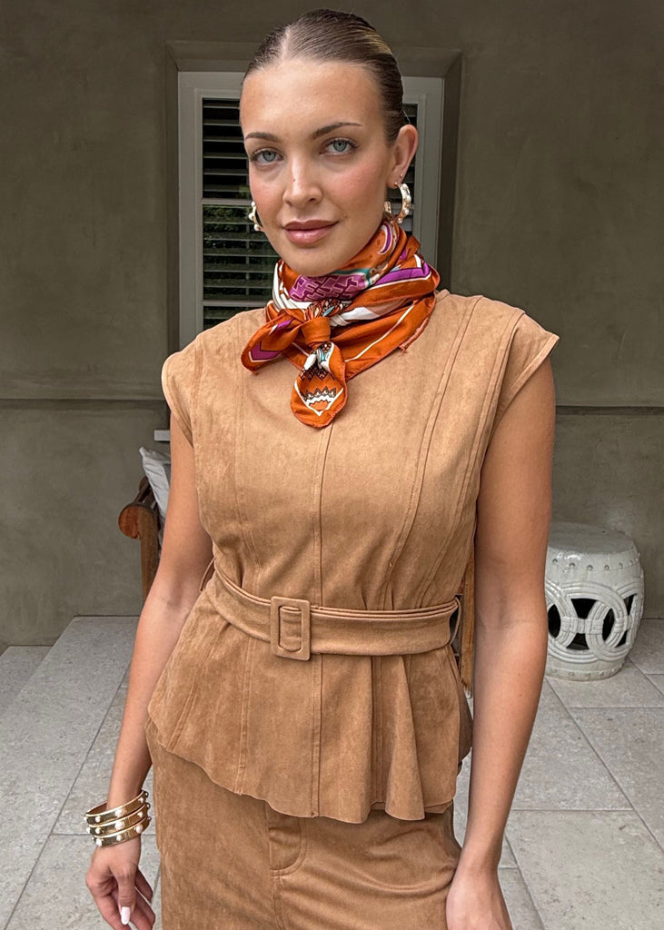 Woman wearing a brown outfit with a colorful scarf, standing outdoors.