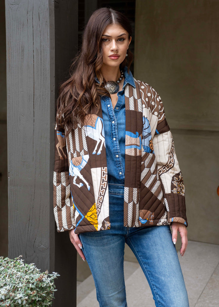 Woman wearing a patterned jacket over a denim shirt and jeans, standing indoors.