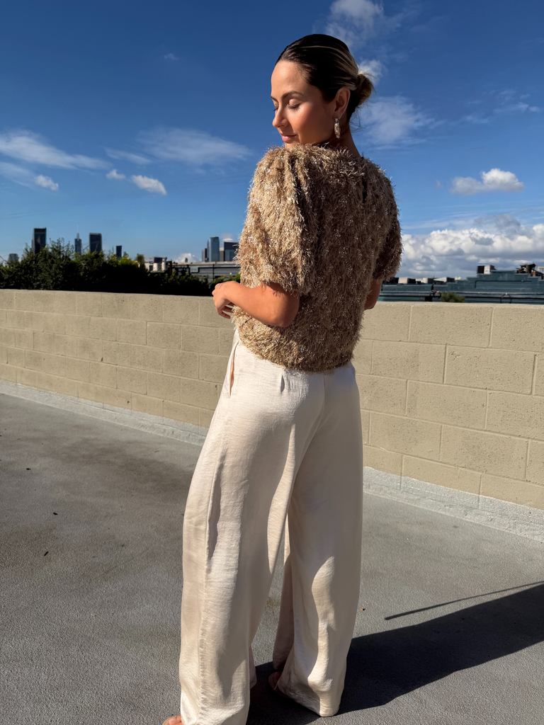 Woman wearing a patterned top and beige pants on a rooftop with a city skyline in the background