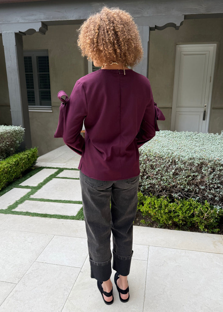 Person wearing a burgundy top and dark pants standing in a garden area.
