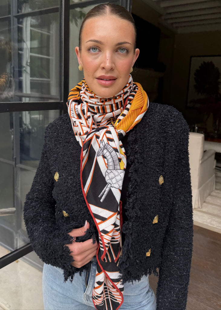 Woman wearing a patterned scarf and black coat standing in front of a building entrance.
