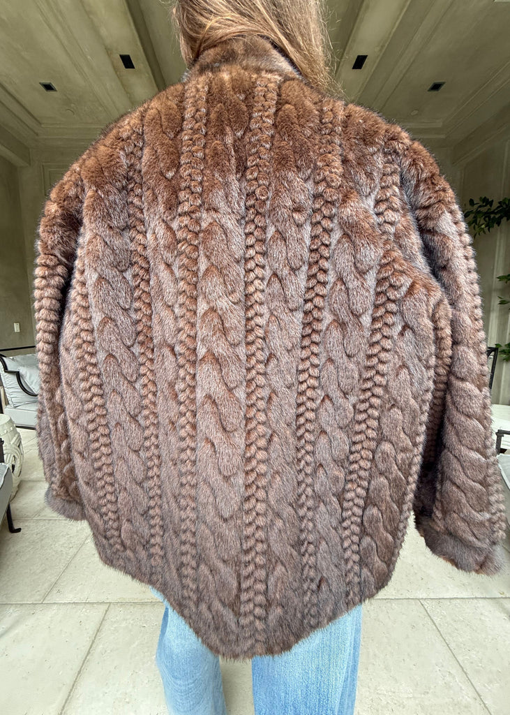 Person wearing a brown knitted sweater with a cable pattern indoors.