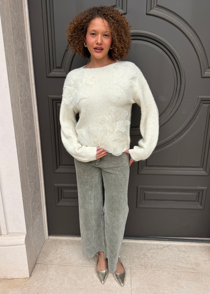 Woman wearing a light green sweater and gray pants standing in front of a dark gray door.