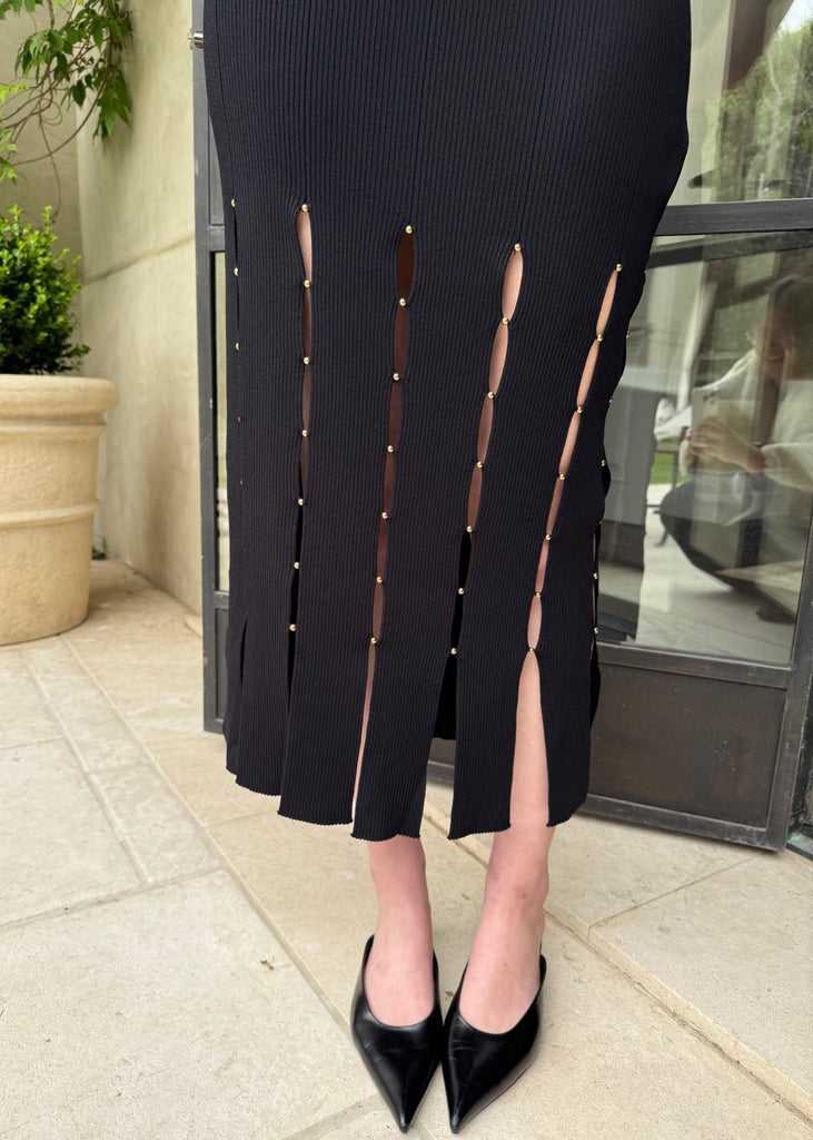 Person wearing a black dress with cut-out sides and black shoes on a sidewalk.