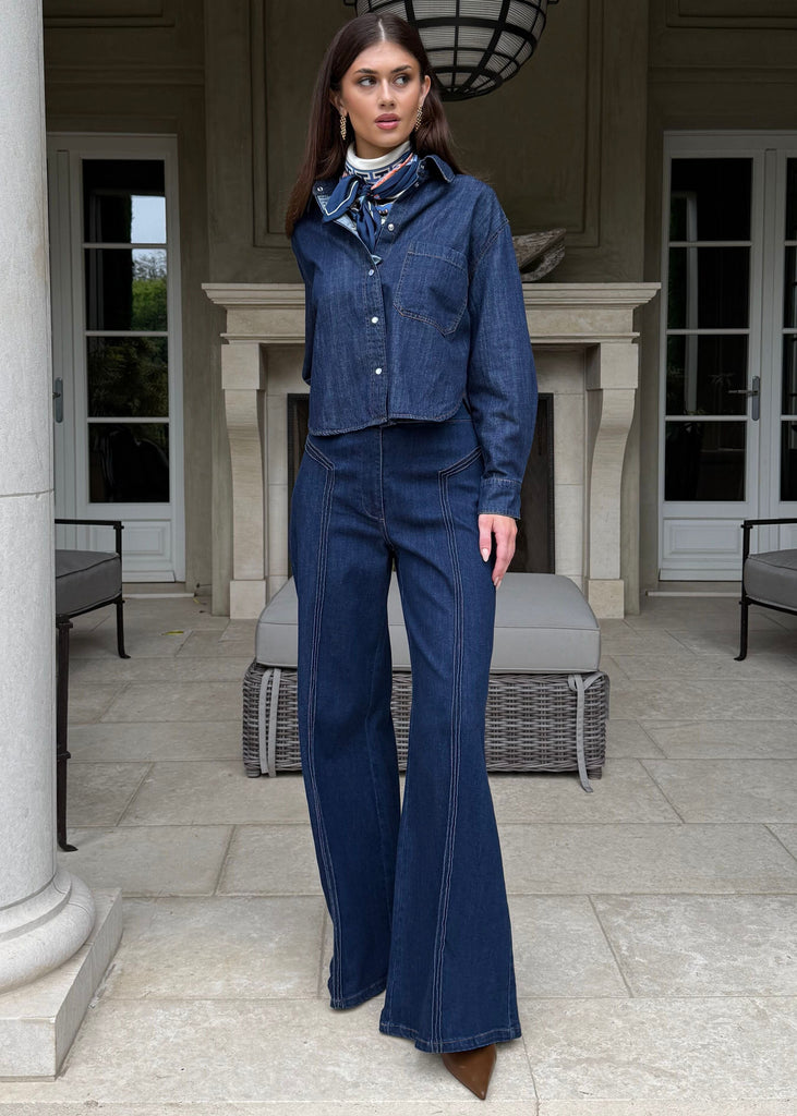 Woman in a blue outfit standing in a classical architectural setting with columns and a fireplace.