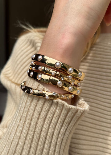 Close-up of a wrist wearing multiple gold and pearl bracelets on a beige sweater.
