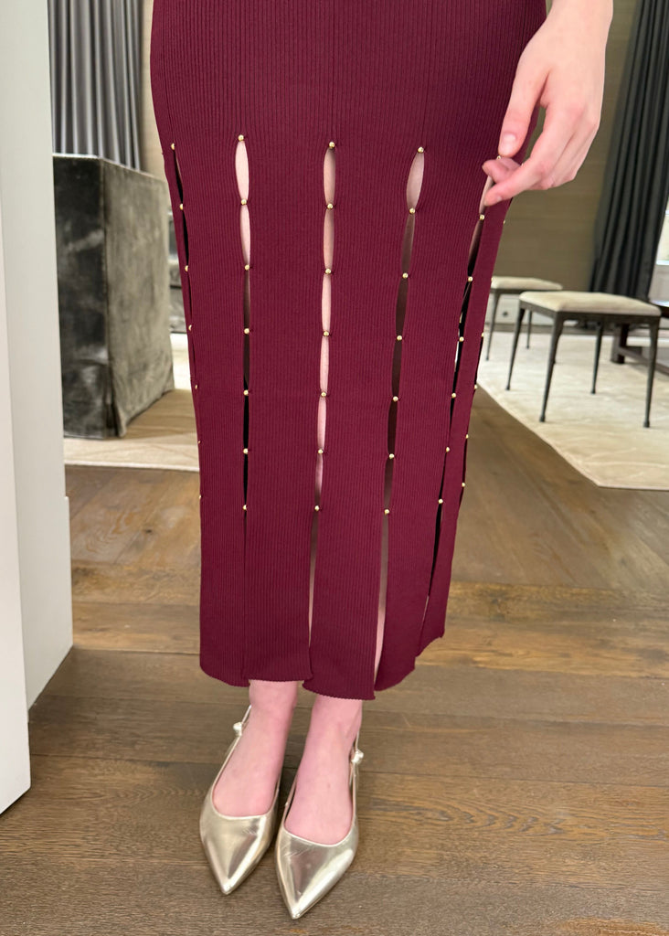 Person wearing burgundy pants with cut-out design in a room with wooden flooring and a window.