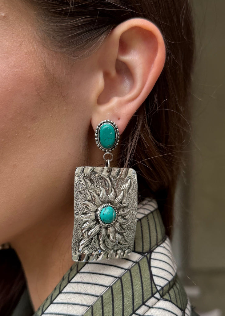 Close-up of a woman wearing a pair of earrings with turquoise stones.