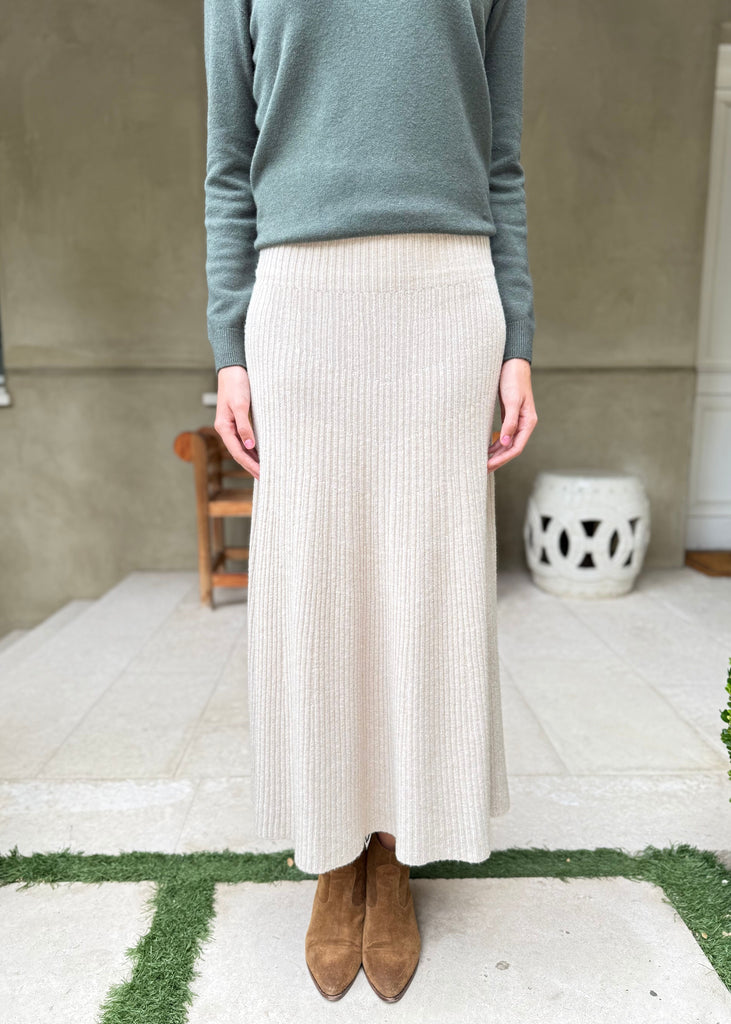 Person wearing a green sweater and beige skirt standing on a patio.