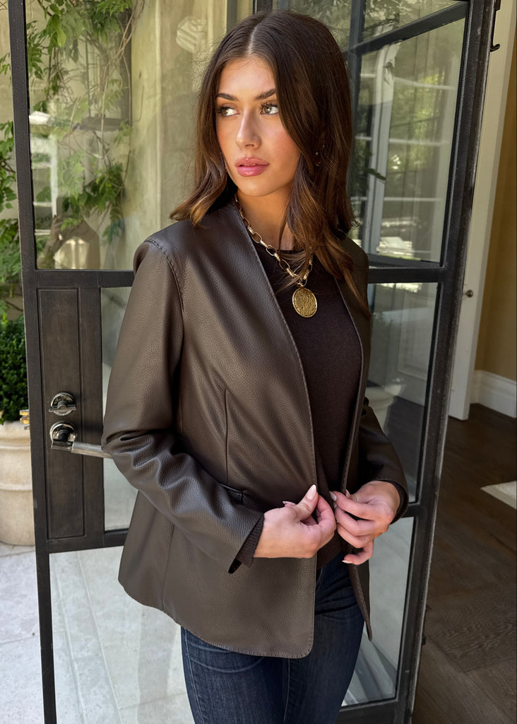Woman wearing a brown blazer and dark top standing in front of a glass door.
