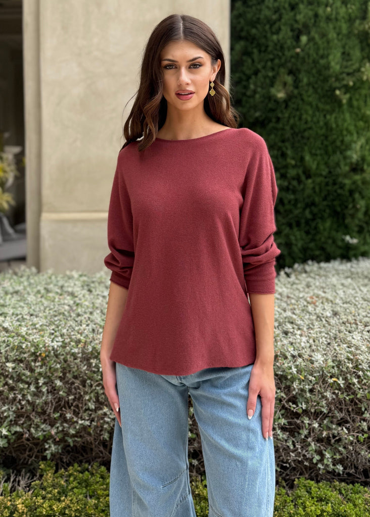 Woman wearing a maroon sweater and light blue jeans standing outdoors.