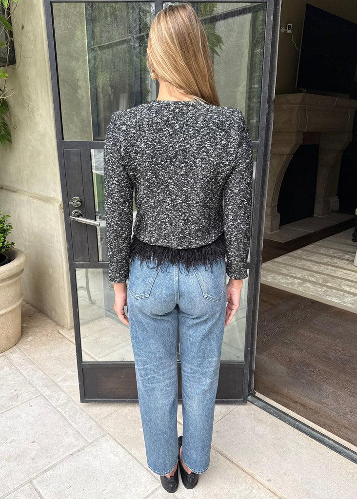 Person wearing a patterned top and jeans standing in front of a glass door.