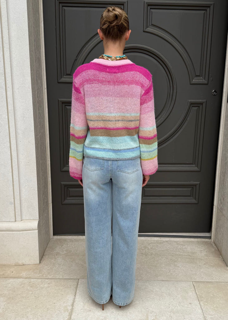 Person wearing a colorful sweater and jeans standing in front of a dark door.