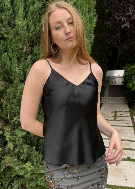 Woman wearing a black satin top and floral skirt standing outdoors.
