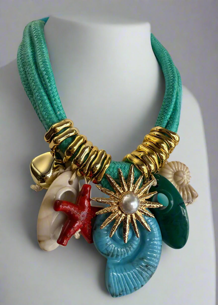 Necklace with gold clasp, starfish, shell, and pearl charm on a mannequin.