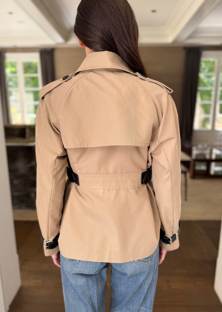 Person wearing a beige trench coat in an indoor setting