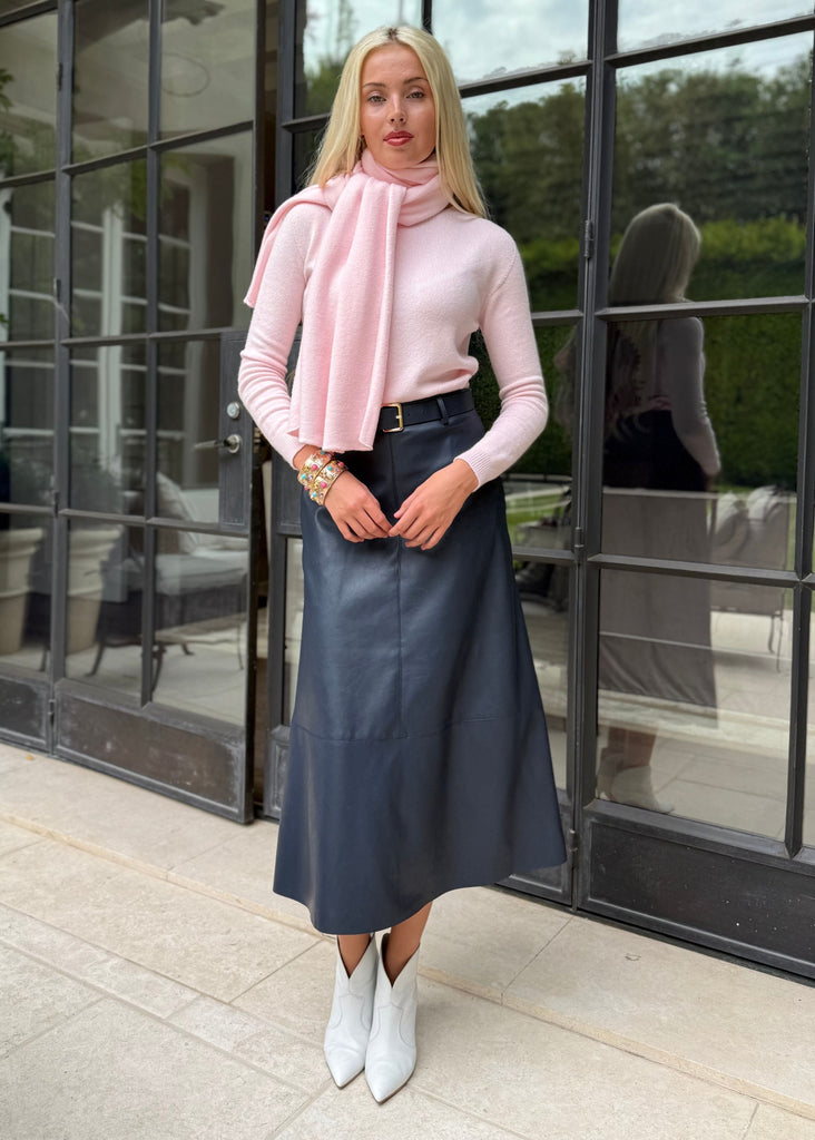 Woman wearing a pink sweater and blue skirt standing in front of a glass door.