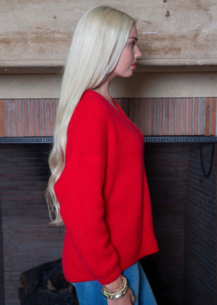 Woman wearing a red sweater and blue jeans standing against a wooden wall.