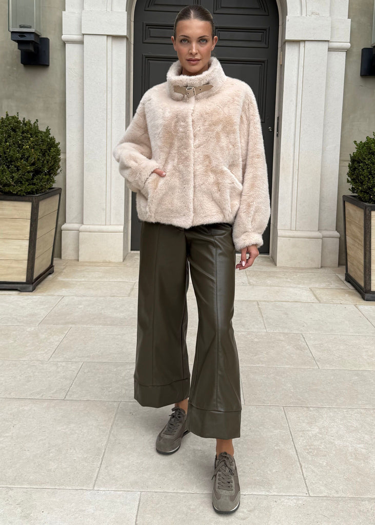 Person wearing a light pink fur coat standing in front of a building entrance.