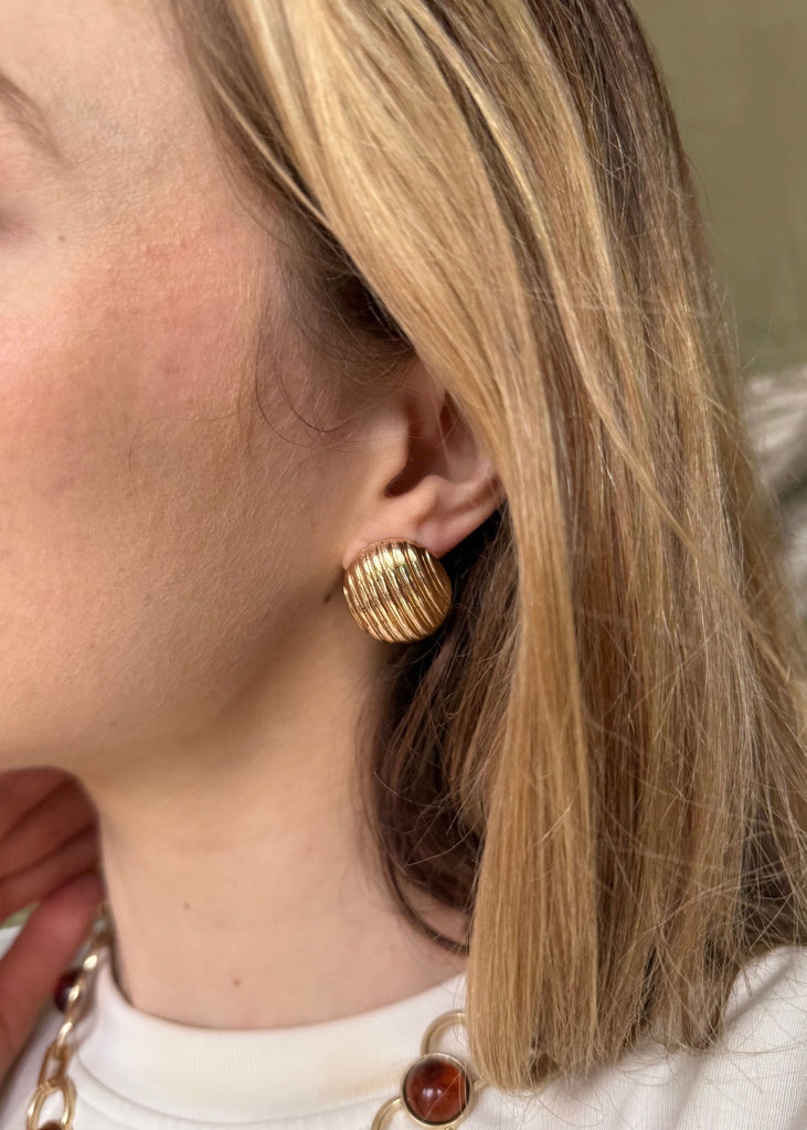 Close-up of a person wearing gold hoop earrings with a neutral background