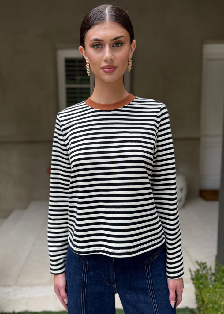 Woman wearing a black and white striped shirt and blue jeans standing in front of a house.