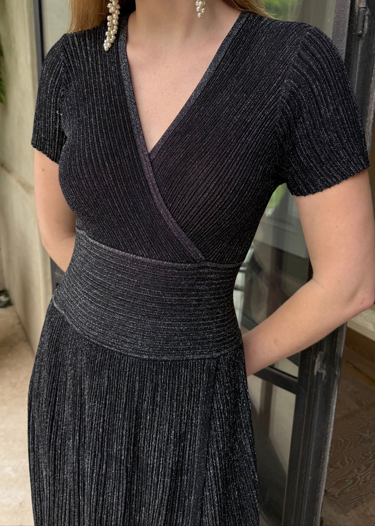 Woman wearing a black ribbed dress with pearl earrings indoors.