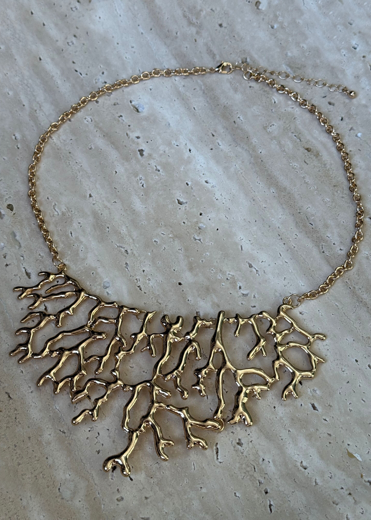 Gold necklace with a leaf-like design on a textured surface