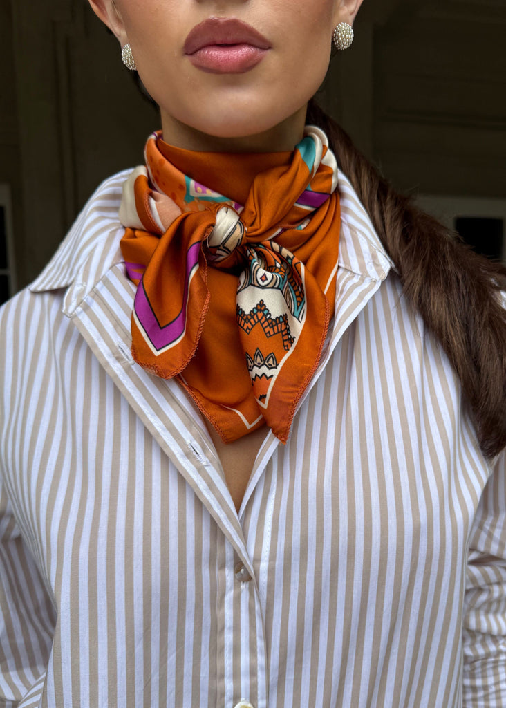 Woman wearing a striped shirt with an orange scarf tied around her neck.