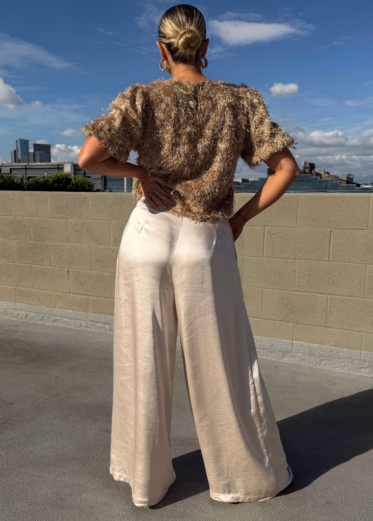 Person wearing a patterned top and beige wide-leg pants on a rooftop with a cityscape in the background.