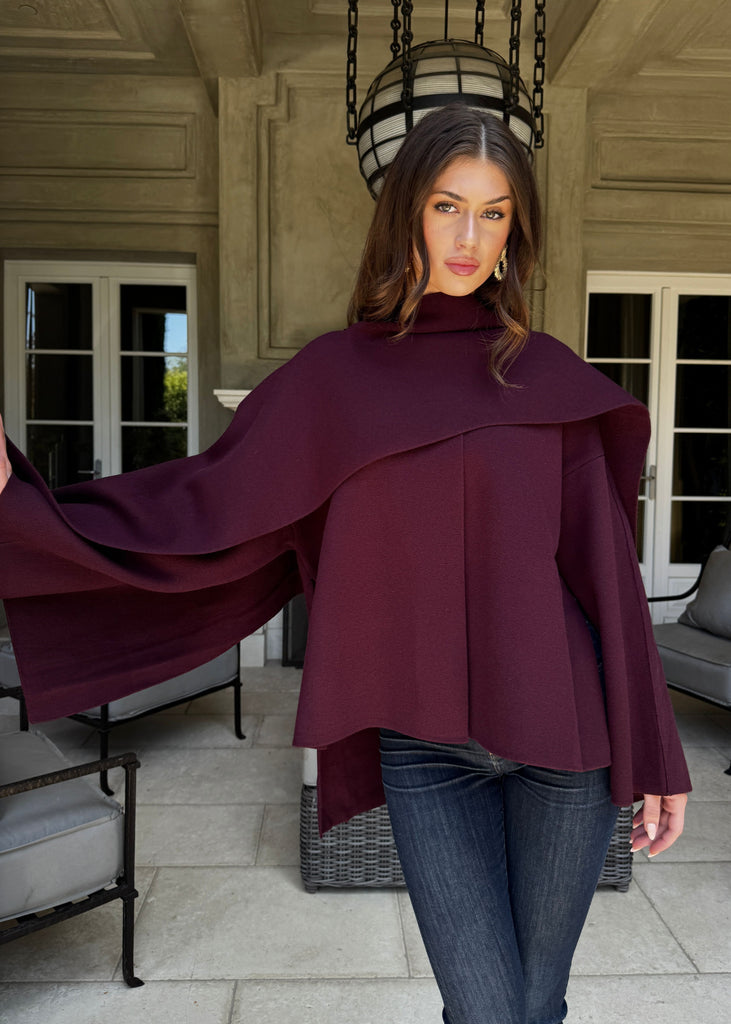 Woman wearing a burgundy cape in an outdoor setting