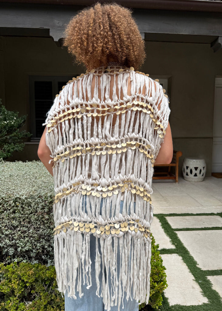 Person wearing a decorative vest with fringe and gold accents in an outdoor setting.