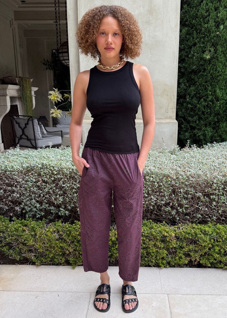 Woman wearing a black sleeveless top and purple pants standing outdoors.