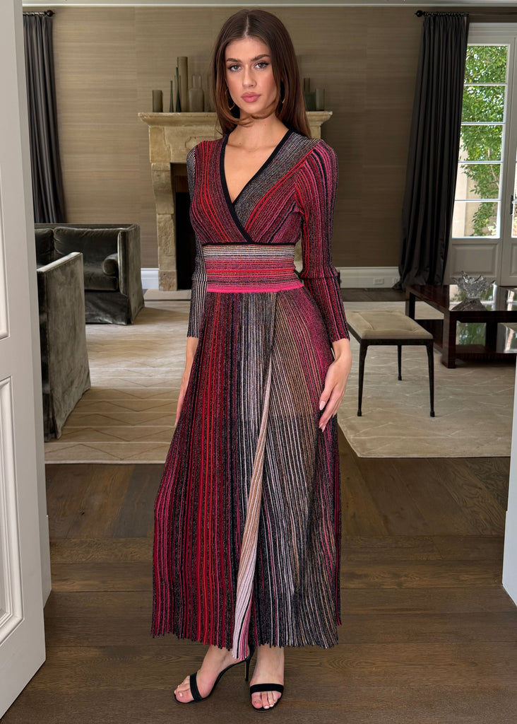 Woman in a long, patterned dress standing in a room with wooden flooring and white walls.