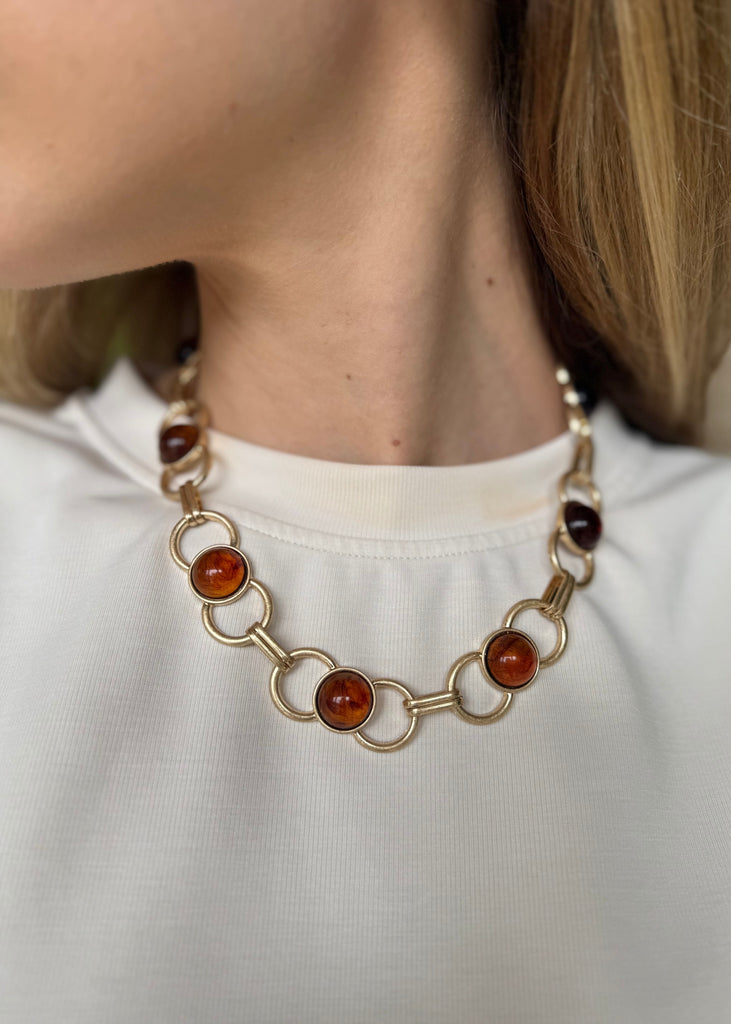 Necklace with amber-colored beads worn by a person on a plain background