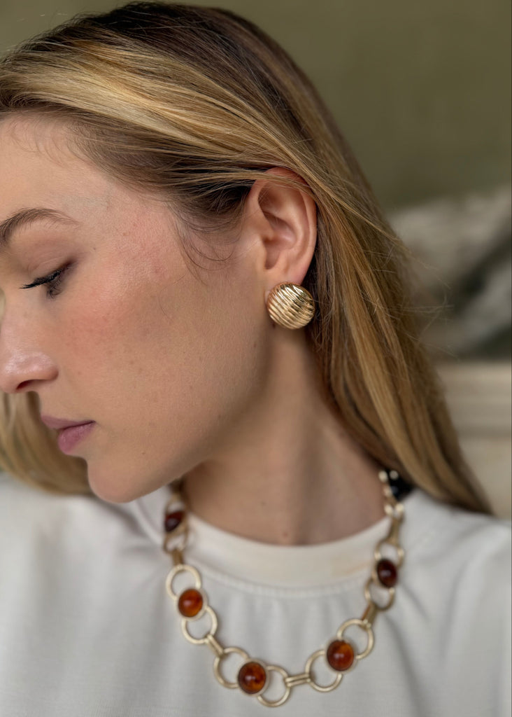 Woman wearing gold earrings and a necklace with a blurred background