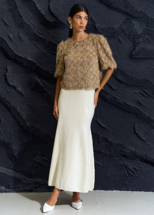 Woman wearing a textured top and white skirt against a black textured wall.