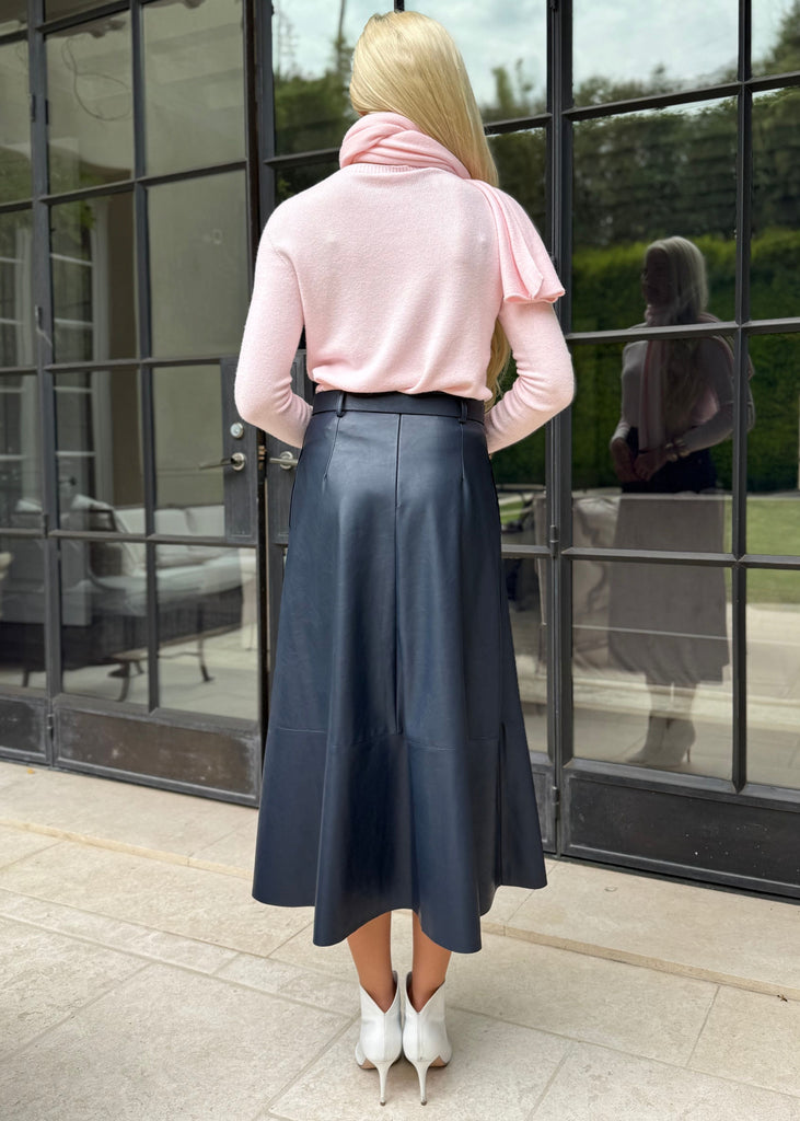 Woman in a pink sweater and blue skirt standing in front of large glass doors.
