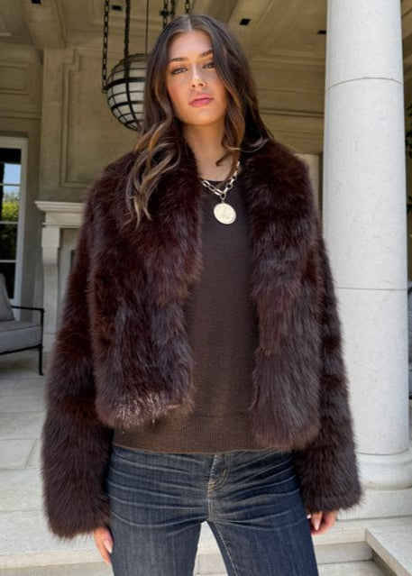 Woman wearing a fur coat standing on a porch with columns.