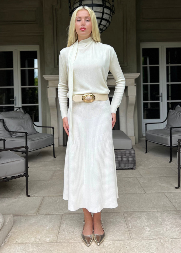 Woman in a white outfit standing on a patio with columns and chairs in the background
