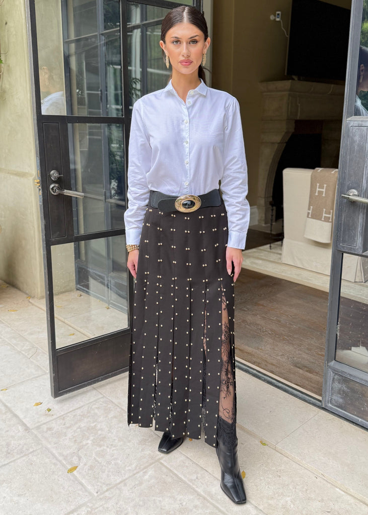 Woman in a white shirt and black patterned skirt standing in front of a glass door.