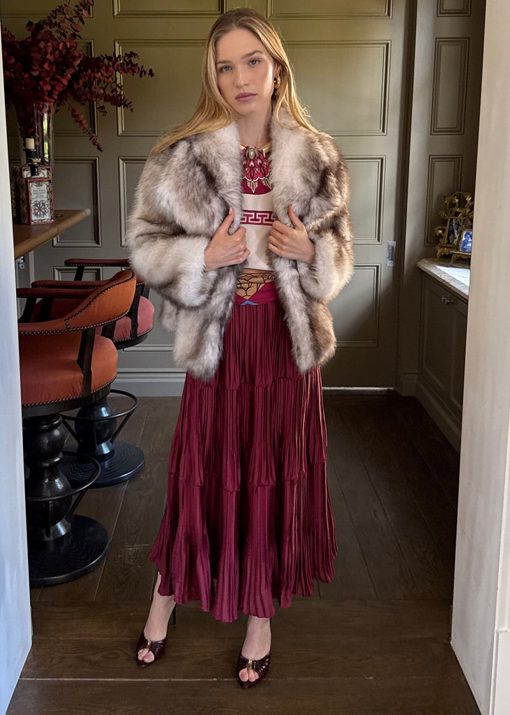 Woman wearing a fur coat and red dress in a room with a mirror.