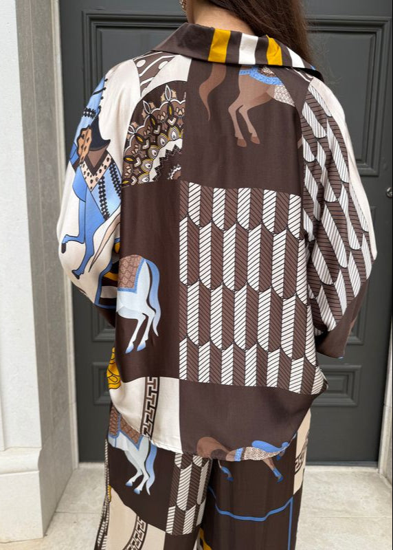 Person wearing a patterned outfit with horses and geometric designs in front of a door.