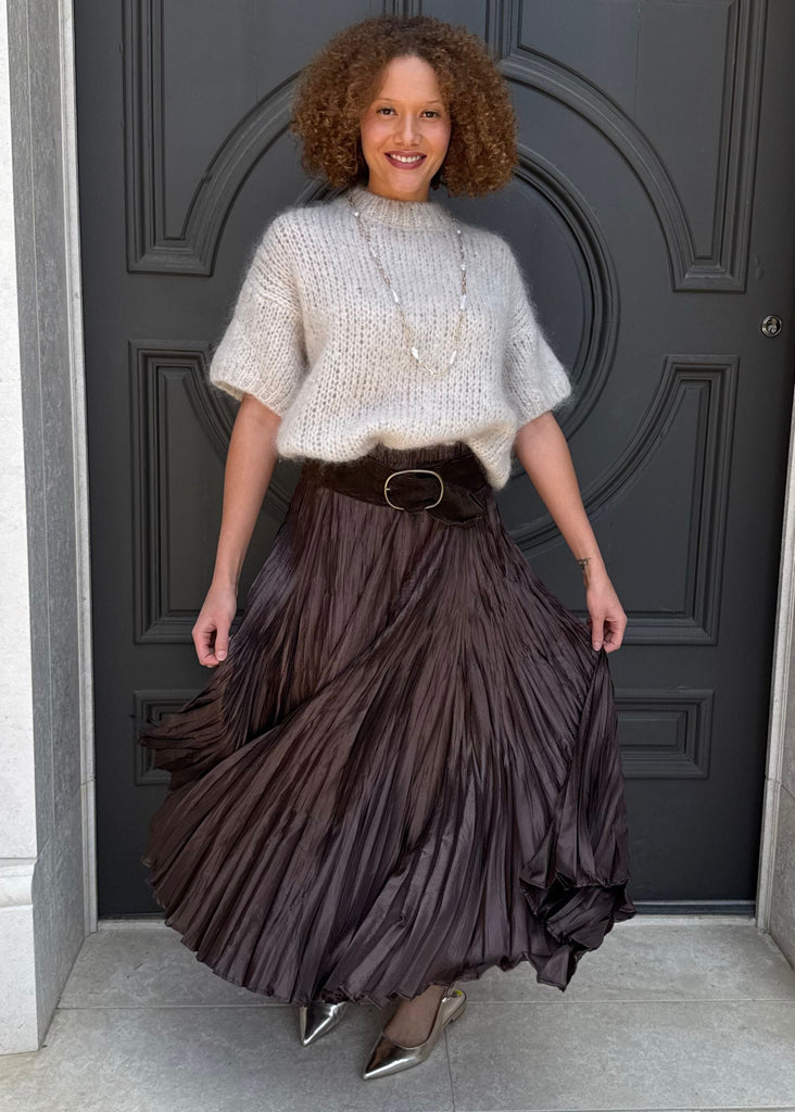 Woman in a white top and dark pleated skirt twirling in front of a large door.