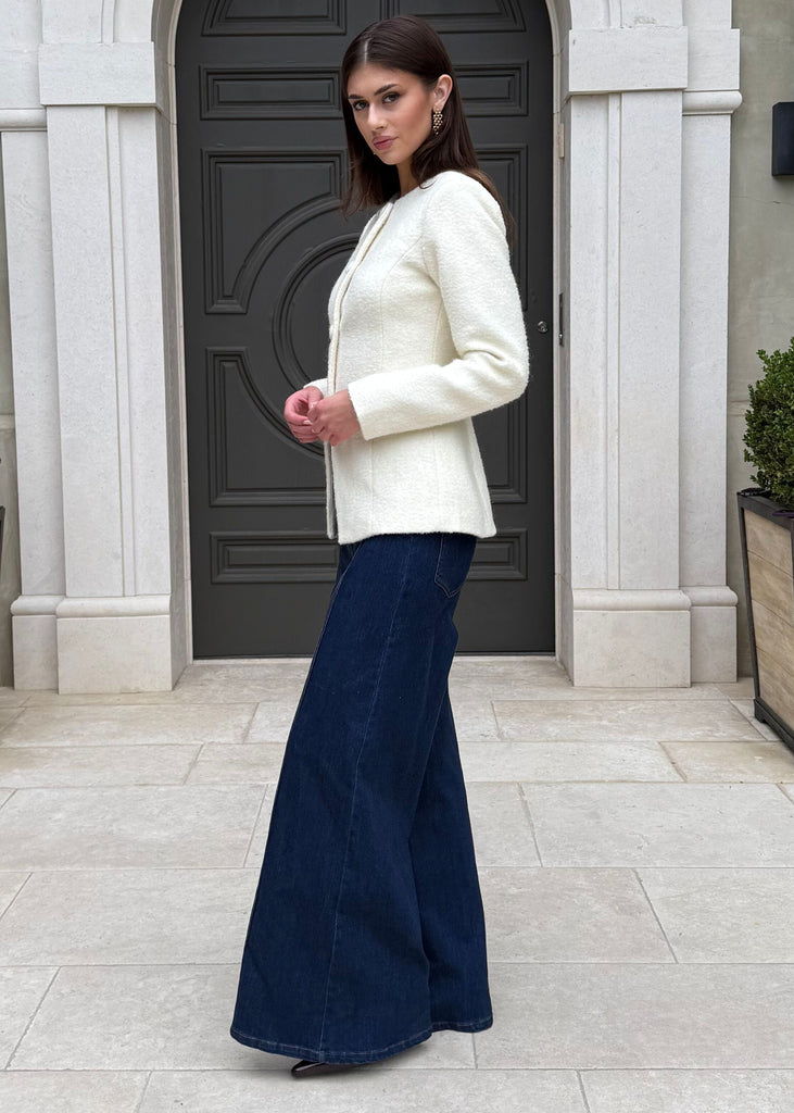 Woman in a white sweater and navy skirt standing in front of a gray door with decorative elements.