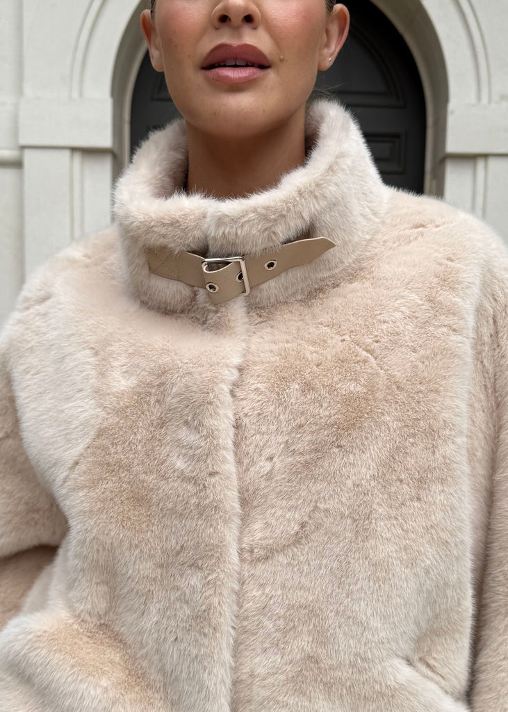 Woman wearing a beige fluffy jacket standing in front of a building entrance.