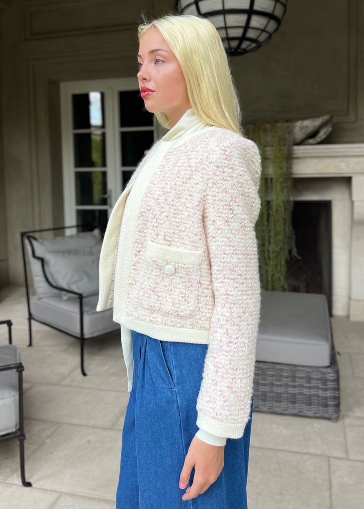 Person wearing a white textured jacket and blue pants standing in an outdoor patio area.