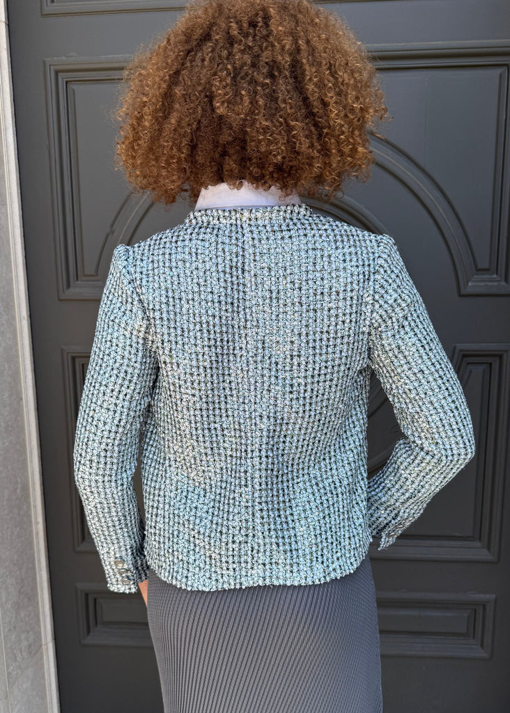 Person wearing a textured blazer and gray skirt standing in front of a dark door.