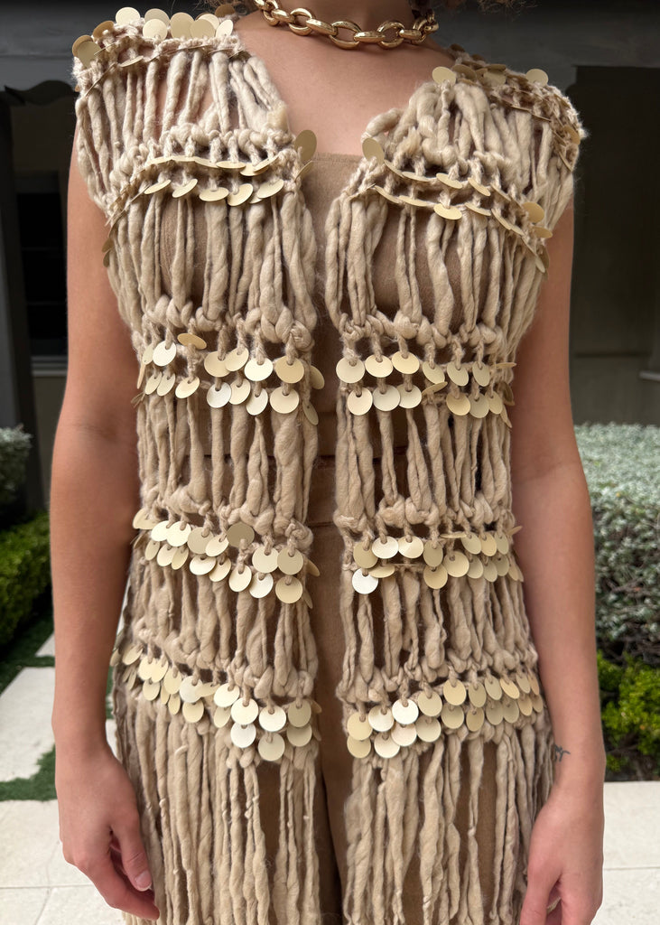 Beige macramé vest with gold accents worn by a person outdoors.