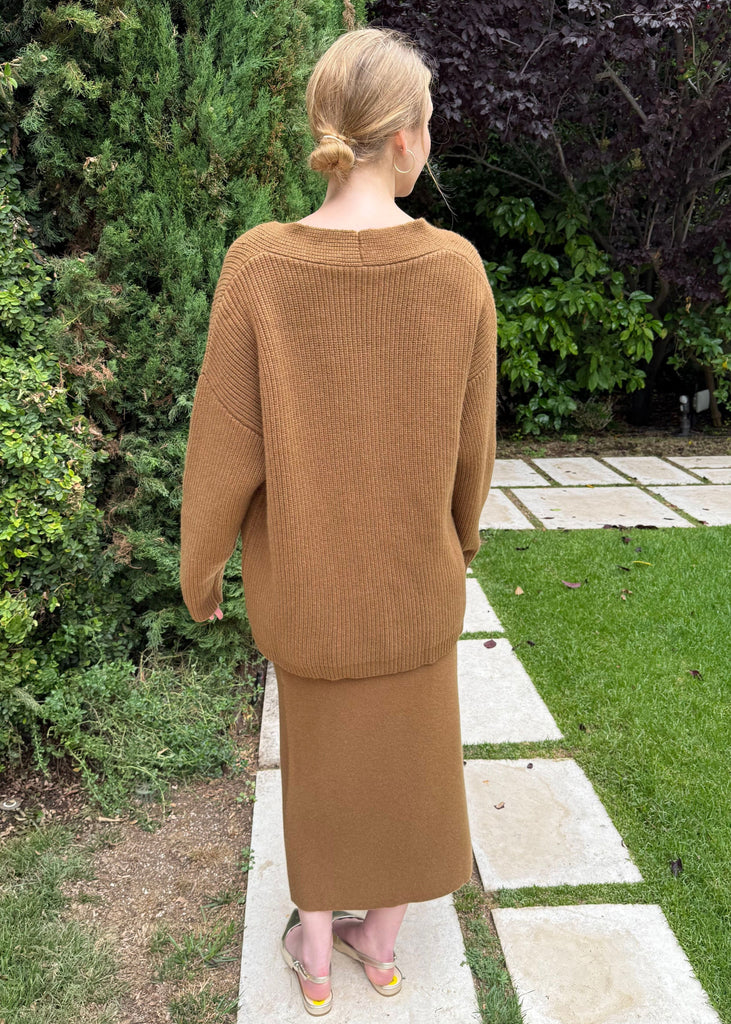 Person wearing a brown outfit walking on a garden path with greenery around.