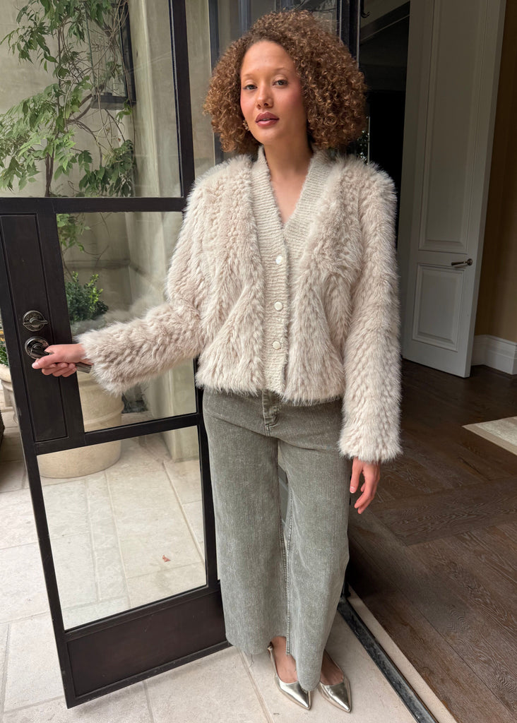 Woman wearing a fluffy white cardigan and light gray pants standing in a doorway.